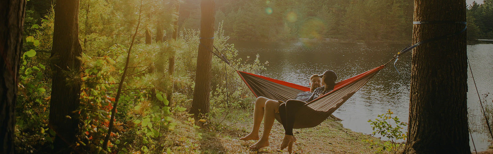 Couple in a hammock on the shore of a small pond in the woods.