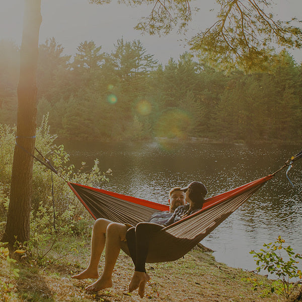 Couple sitting in hammock on the shore of a small lake located in the woods