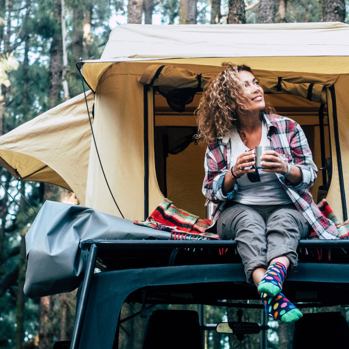 Cozy woman camping in a topper tent in colorful socks drinking coffee.